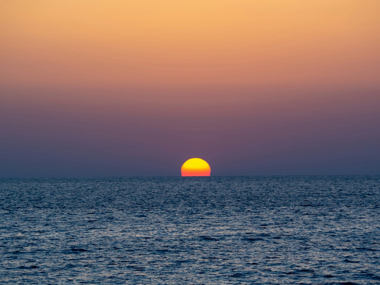 a sunset over the ocean with a boat in the distance
